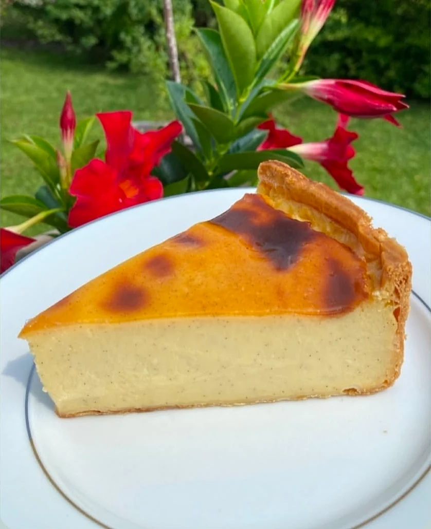 Une part de flan vanille de la Boulangerie Hubert, sur une assiette blanche, dans un jardin.